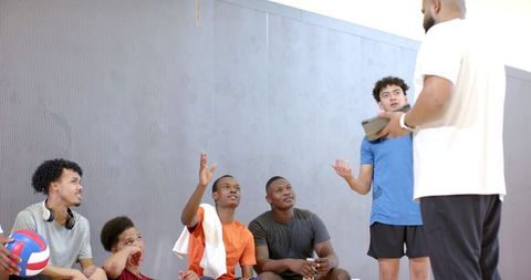 Youth volleyball team listening to coach holding tablet on bench during indoor training