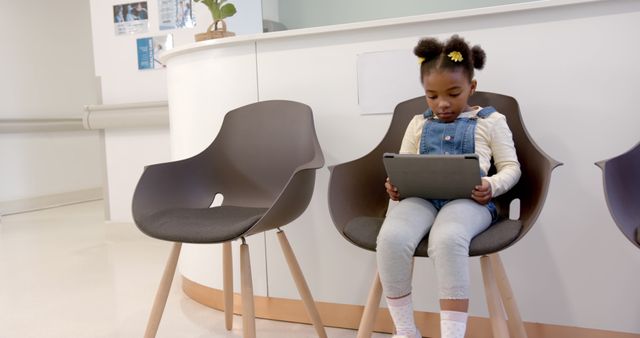 African american girl patient using tablet sitting in waiting room in hospital, copy space. Medicine, healthcare, communication and hospital, unaltered.