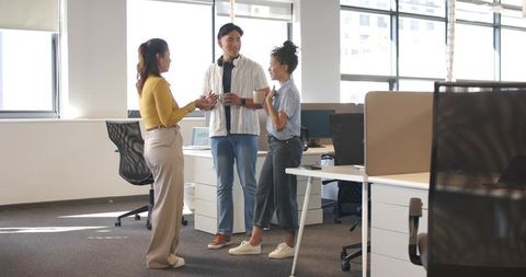Young diverse coworkers chatting over coffee in bright modern open-plan office