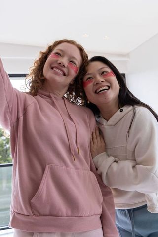 Friends smiling with under-eye patches wearing cozy hoodies home self-care moment