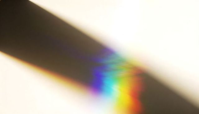 Diagonal shadow casting vibrant prism rainbow burst on pale background abstract design