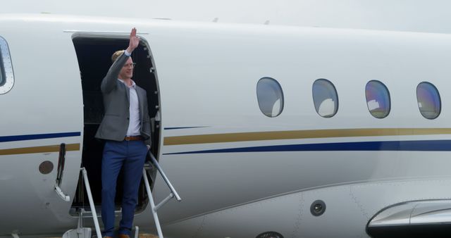 Businessman waving while boarding a private jet shows themes of executive and luxury travel. Ideal for use in corporate advertising, travel promotions, and articles about business or private aviation.