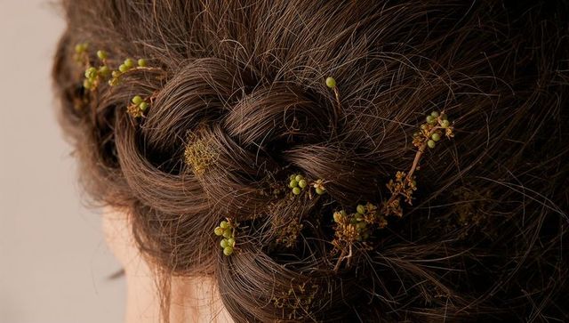 Braided chestnut hair woven with green buds and dried wildflower sprigs