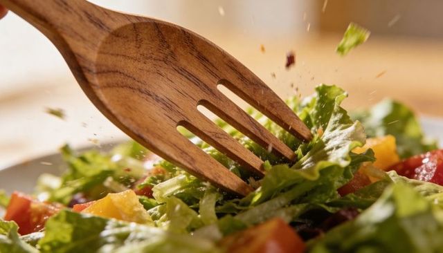 Tossing fresh romaine salad with wooden fork and vinaigrette sprinkles, dynamic closeup action