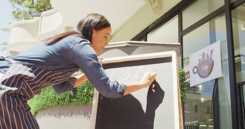 Smiling waitress writing daily special on cafe blackboard