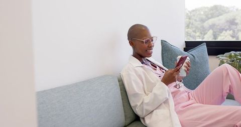 African healthcare professional relaxing on clinic sofa on break with smartphone and coffee