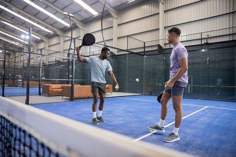 Indoor padel training with diverse male friends on blue court in covered sports club