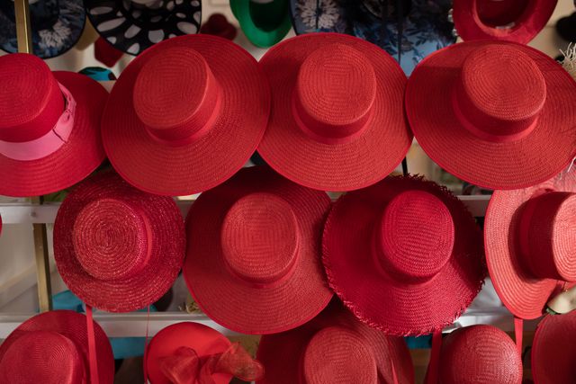 Front view of various styles of red hats for women displayed in rows on the white walls of the showroom at a hat makers. 