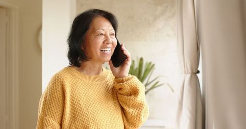 Senior woman smiling while chatting on smartphone indoors