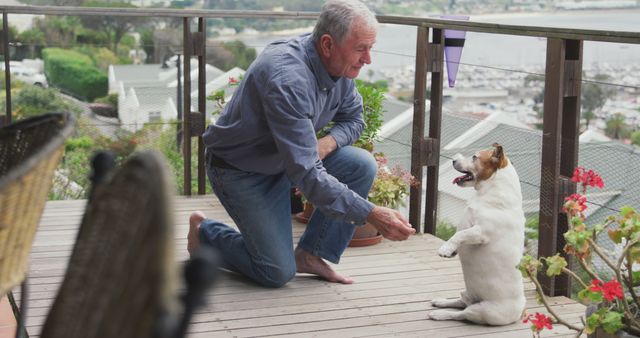 Senior man on deck training a Jack Russell Terrier with scenic ocean view in background. Ideal for use in advertisements focusing on senior activities, pet training, outdoor hobbies, retirement lifestyle, and nature enjoyment. Shows positive everyday life in a coastal or seaside area.