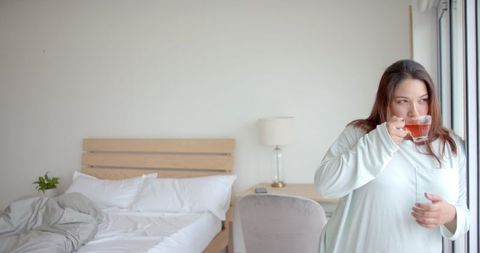 Plus Size Biracial Woman Enjoying Tea by Bedroom Window