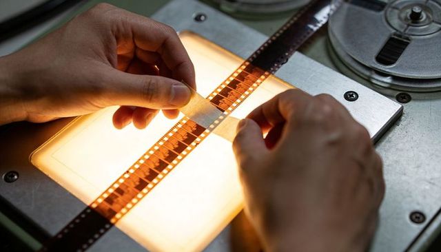 Hands splicing 35mm film on lightbox for archival digitization and restoration closeup