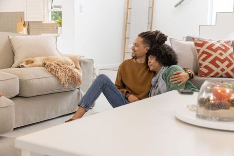 African american couple relaxing on floor leaning against sofa with sleeping dog
