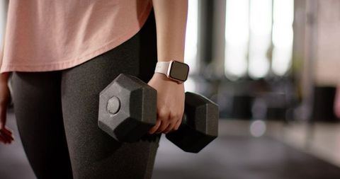 Female athlete holding hex dumbbell wearing smartwatch and leggings during strength workout