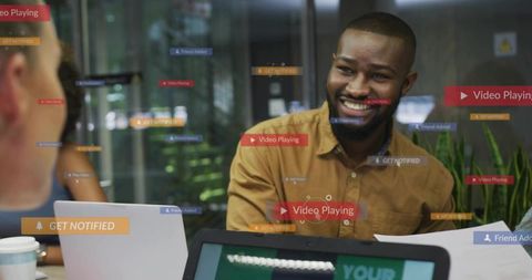 Smiling man leading collaborative tech meeting with laptops and digital ui overlays