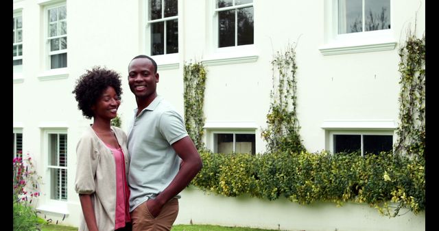 Couple is enjoying quality time outside modern house with lush greenery in background. Perfect for real estate promotions, lifestyle blogs, family-related content, or adverts for home and garden products.