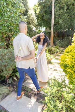 Man hiding flower behind back while couple holding hands on garden stepping-stone path