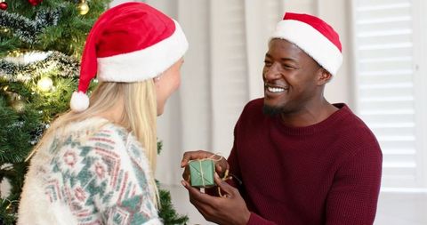 Diverse Couple Sharing Gift by Christmas Tree in Festive Setting