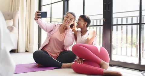 African american friends taking yoga selfie at home in activewear on sunlit balcony