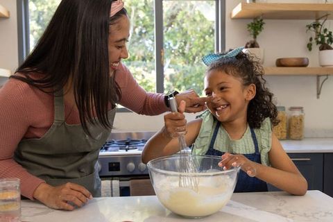 Mother guiding daughter whisking batter in sunny family kitchen
