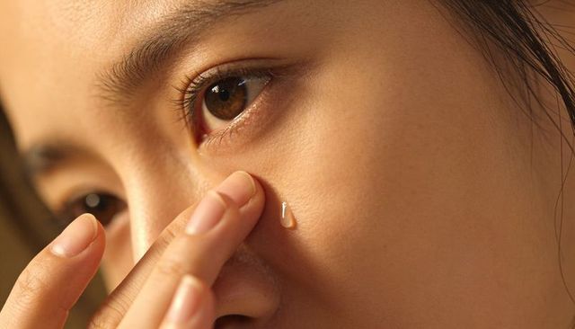 Closeup asian woman wiping teardrop with fingertips warm skincare portrait emotion