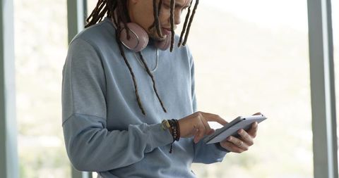 African american man tapping tablet by window wearing pink headphones and dreadlocks