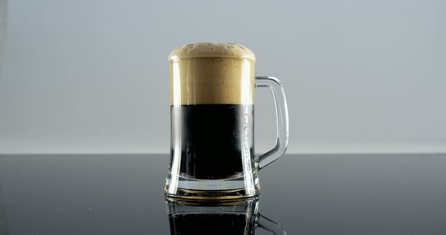 Glass mug filled with dark stout beer showcasing frothy head, perfect for promoting breweries, pubs, bars, and alcoholic beverages. Suitable for use in marketing materials, ads, menus, and social media posts related to beer and brewing industry.