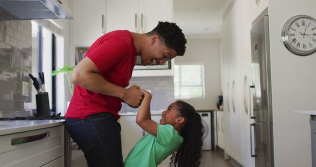 Happy biracial father and daughter dancing together in kitchen in kitchen. domestic lifestyle, spending free time at home.