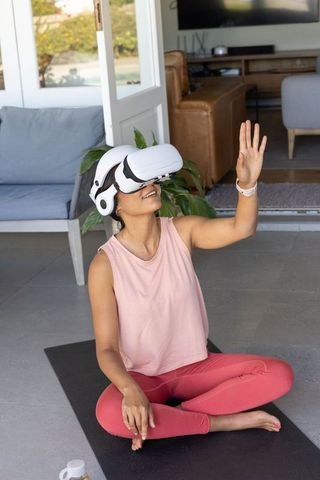 African woman practicing virtual yoga with vr headset and headphones for home mindfulness