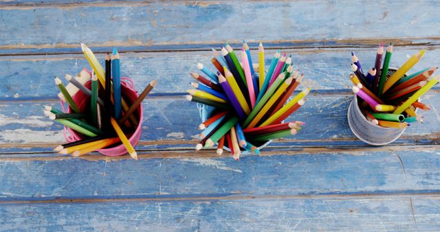 Colorful pencils are arranged in containers on a rustic blue wooden surface, with copy space. The vibrant array of pencils suggests a creative or educational setting, in an art class or a craft workshop.