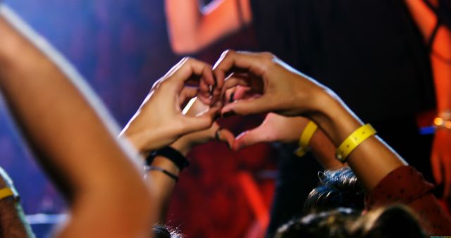 Audience members showing love and excitement at a concert by making heart shapes with their hands. The image captures the vibrant, energetic atmosphere of a live music event, making it perfect for promotional materials, concert advertisements, and articles about music and entertainment culture.