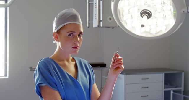Female surgeon holding surgical instrument under overhead light in operating room. Ideal for healthcare, medical training, surgical procedures, hospital environment, brochures, medical websites, and educational materials.