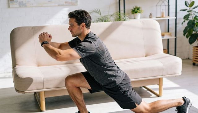 Man performing forward lunge workout in sunlit living room wearing smartwatch minimal home gym