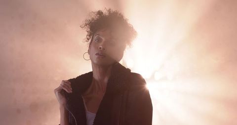 Backlit fashion portrait capturing shearling jacket collar, hoop earring, amber halo studio