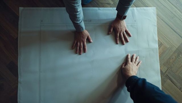 Two professionals leaning over blueprint on parquet floor planning construction project