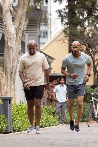 Two african american men walking and jogging together on neighborhood path