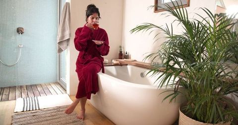 Asian woman in bathrobe relaxing with tea in luxury bathroom