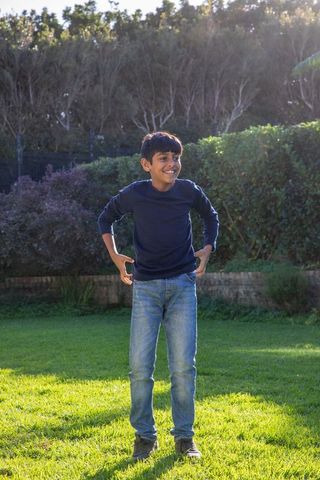 Joyful indian boy standing in sunlit backyard garden