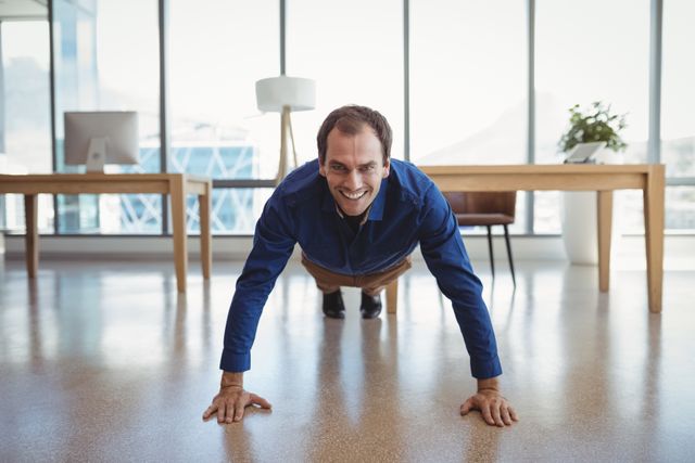 Portrait of smiling executive doing push-ups in office