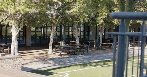Shaded campus courtyard with picnic benches overlooking turf sports field and glass facade