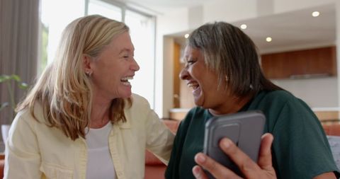 Diverse women laughing at something funny on tablet in living room