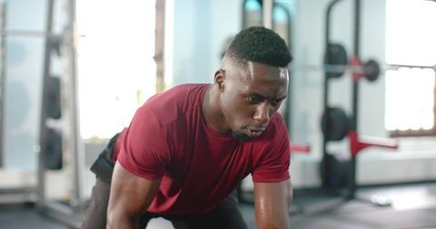 African American man performing intense floor workout in gym with squat rack background