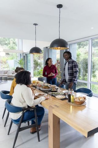 African American Family Sharing Meal at Wooden Dining Table in Modern Glass-Walled Home