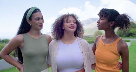 Three african american friends embracing outdoors laughing together on sunny hillside