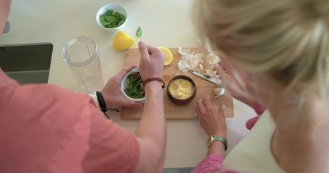 Teenage couple preparing fresh herb dressing together using blender cup and garlic