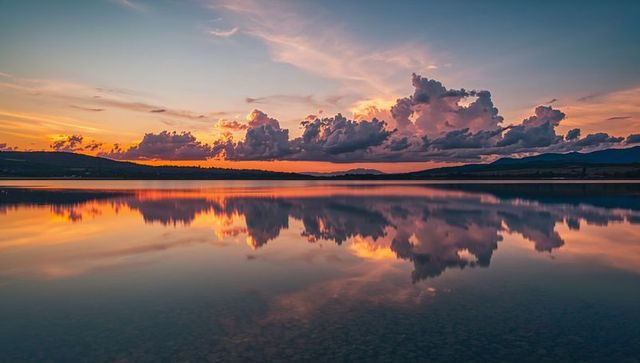 Vibrant sunrise reflections on tranquil lake with dramatic clouds