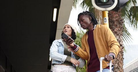 Young diverse travelers checking smartphone for directions at transit stop with luggage