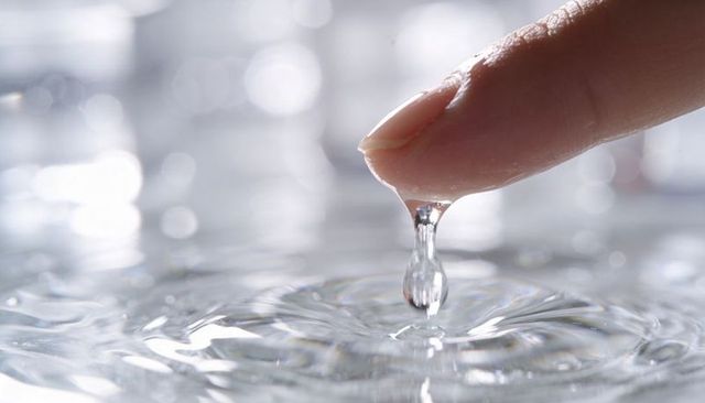 Touching fingertip creating crystal water droplet and ripples with silvery bokeh