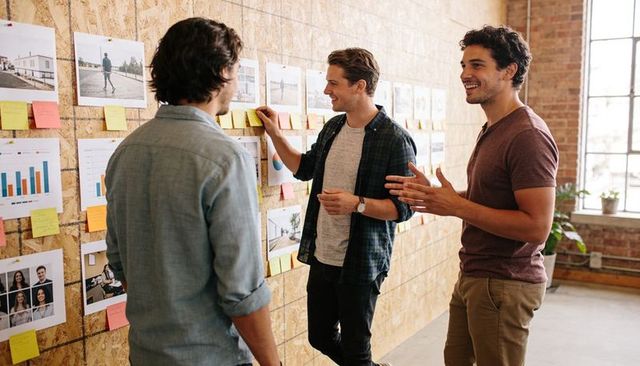 Creative team brainstorming with sticky notes on plywood wall in bright loft office