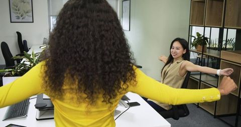Diverse female coworkers stretching at office desks for wellness